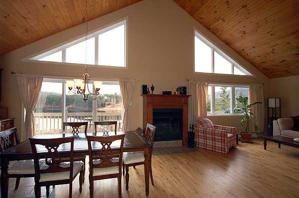 A rustic dining area with an open fireplace, hardwood floors, and large windows revealing a scenic outdoor view and a chandelier.