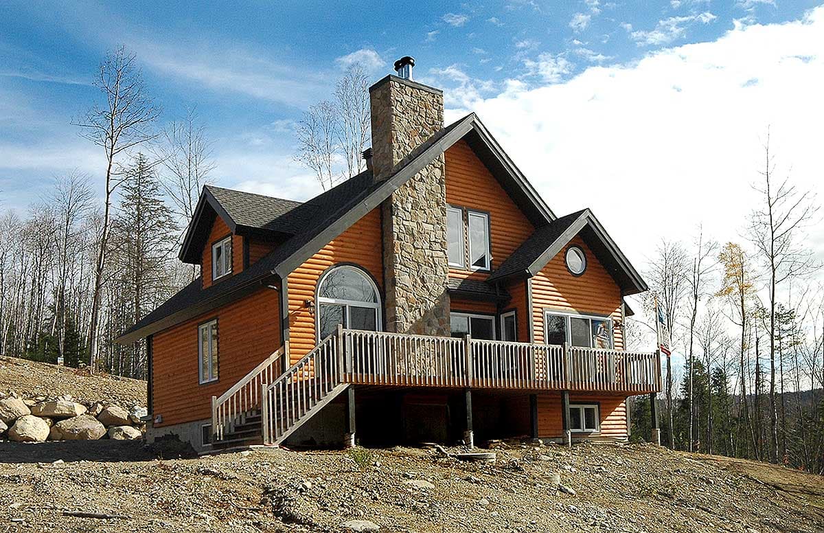 House plan exterior: Two-story log home with stone chimney, large deck, and prominent arched window.