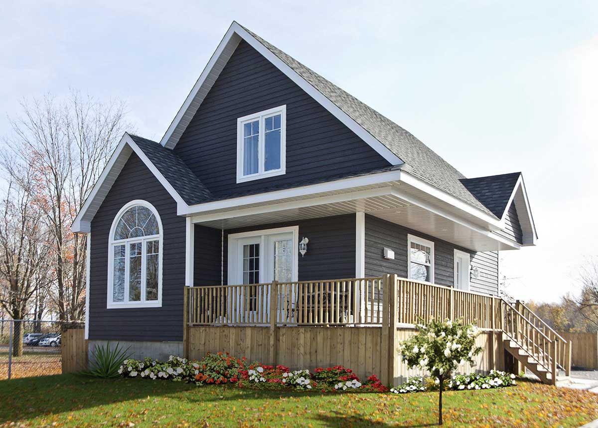 House plan exterior: Dark siding, gabled rooflines, a rounded arched window, and a wraparound wooden deck with stairs.