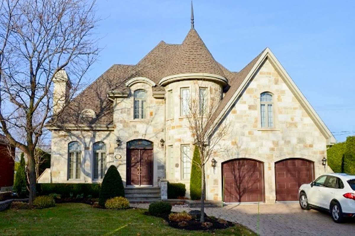 House plan exterior: Two-story stone home with turret, arched dormers, pitched gables, and dual garage.