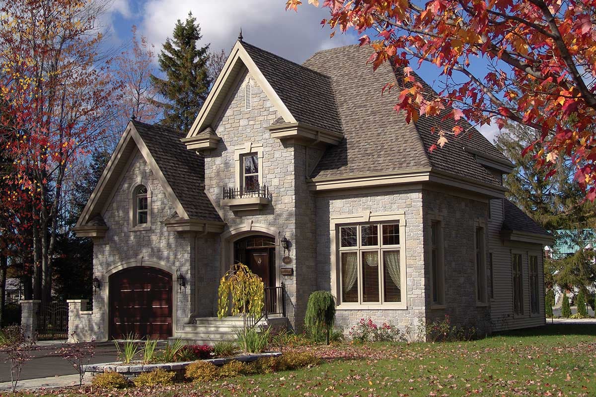 House plan exterior with stone facade, arched garage, dormers, and multiple gables.
