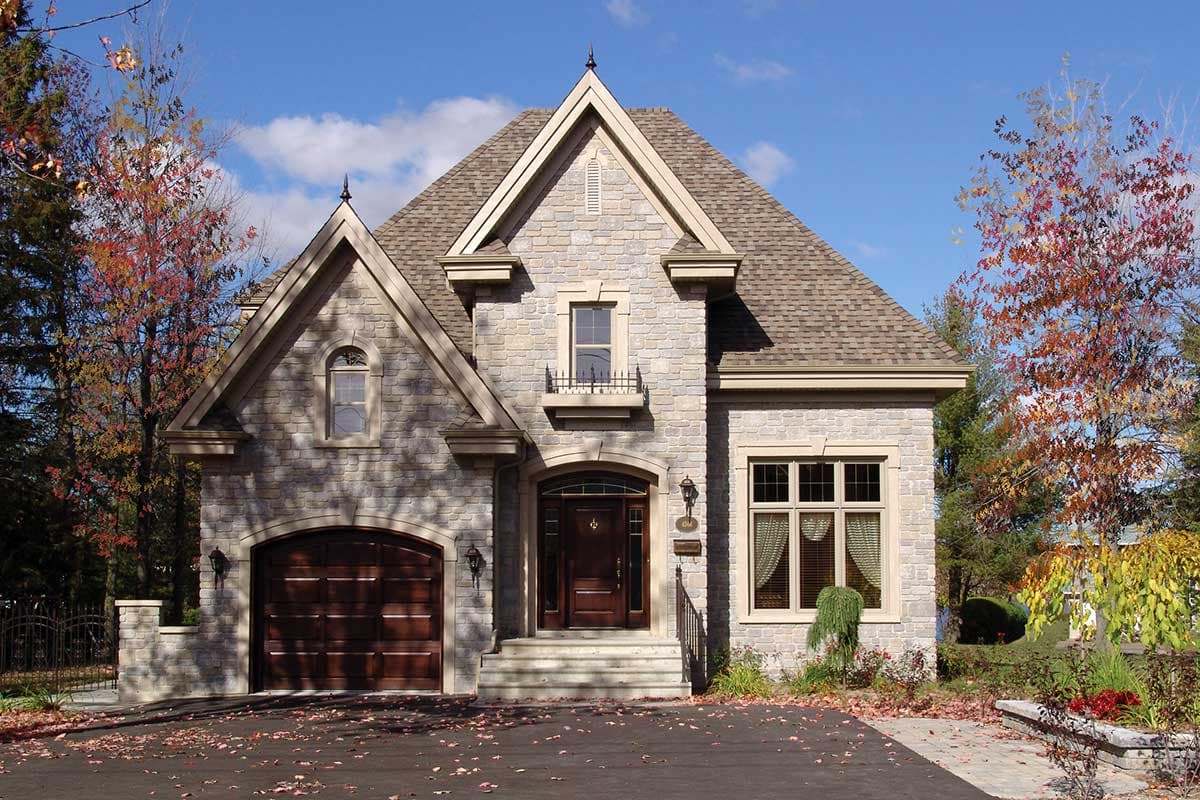 House plan exterior. Two-story stone-clad home with gabled roof, arched entry, and attached garage. Includes dormers and eyebrow windows.
