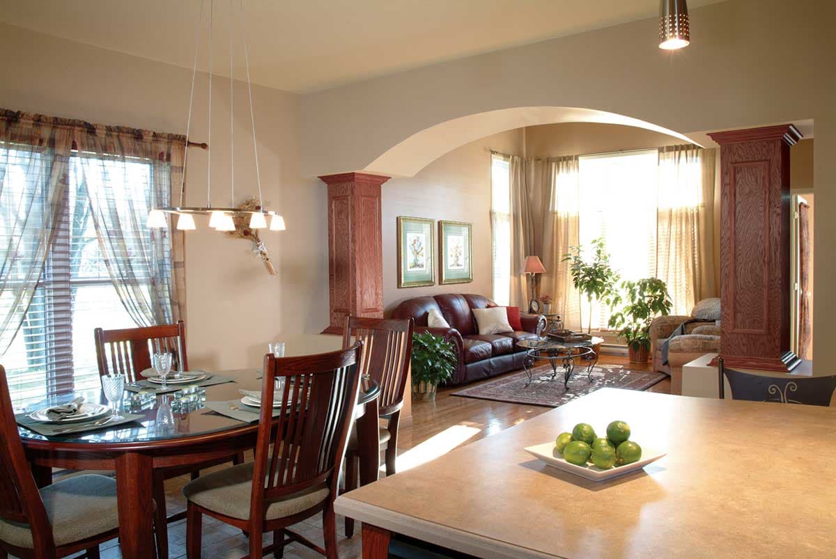 Open concept living area with dining, seating, and kitchen island. Archway connects rooms. Dark wood furniture.