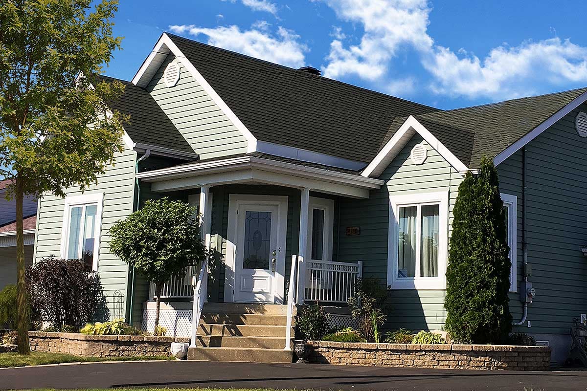 House plan exterior: Two-story house with a front porch, gabled dormers, and light green siding.