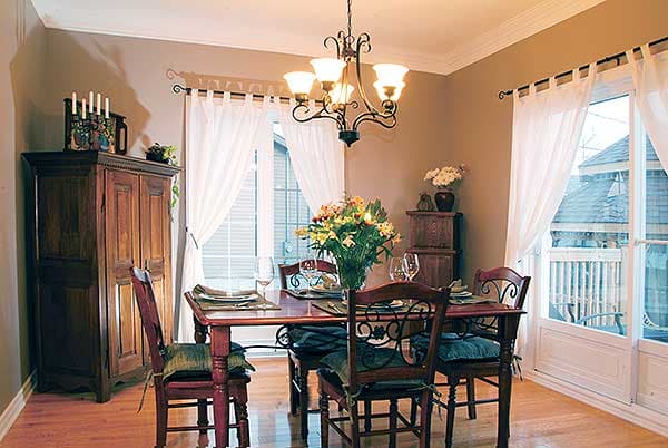 Dining room with a wooden table set for four, tall hutch, and large windows with white curtains.