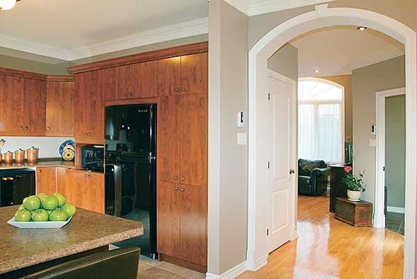Interior view of a kitchen with wood cabinets, black appliances, and an arched entryway to a hallway with hardwood floors.