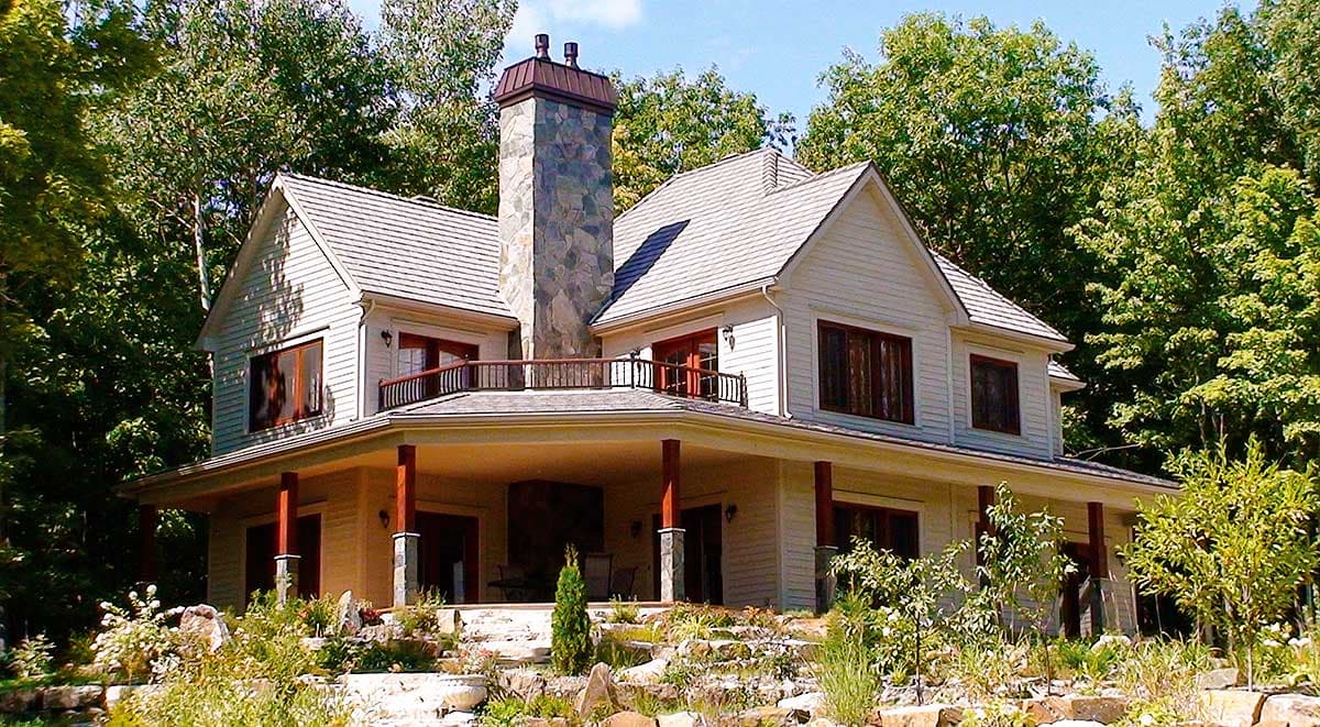 House plan exterior: Two-story home with a wrap-around porch, prominent stone chimney, and multiple gables.