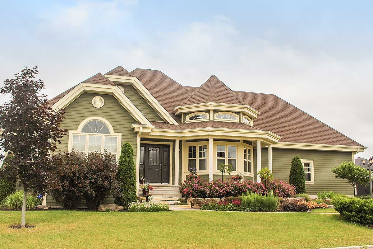 House plan exterior: Green siding, prominent gables, arched window, bay window with octagonal roof, and covered entry.