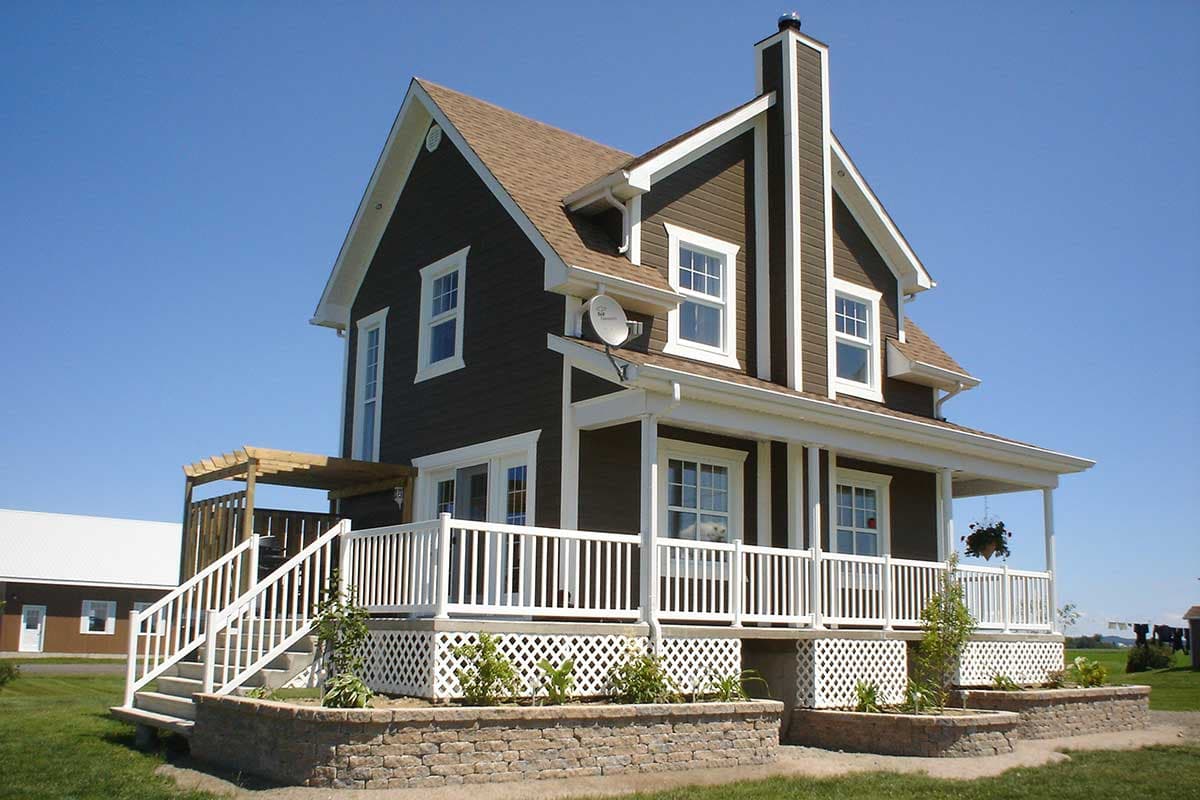 House plan exterior of a two-story Modern Farmhouse with wrap-around porch, prominent gables, and a stone retaining wall.