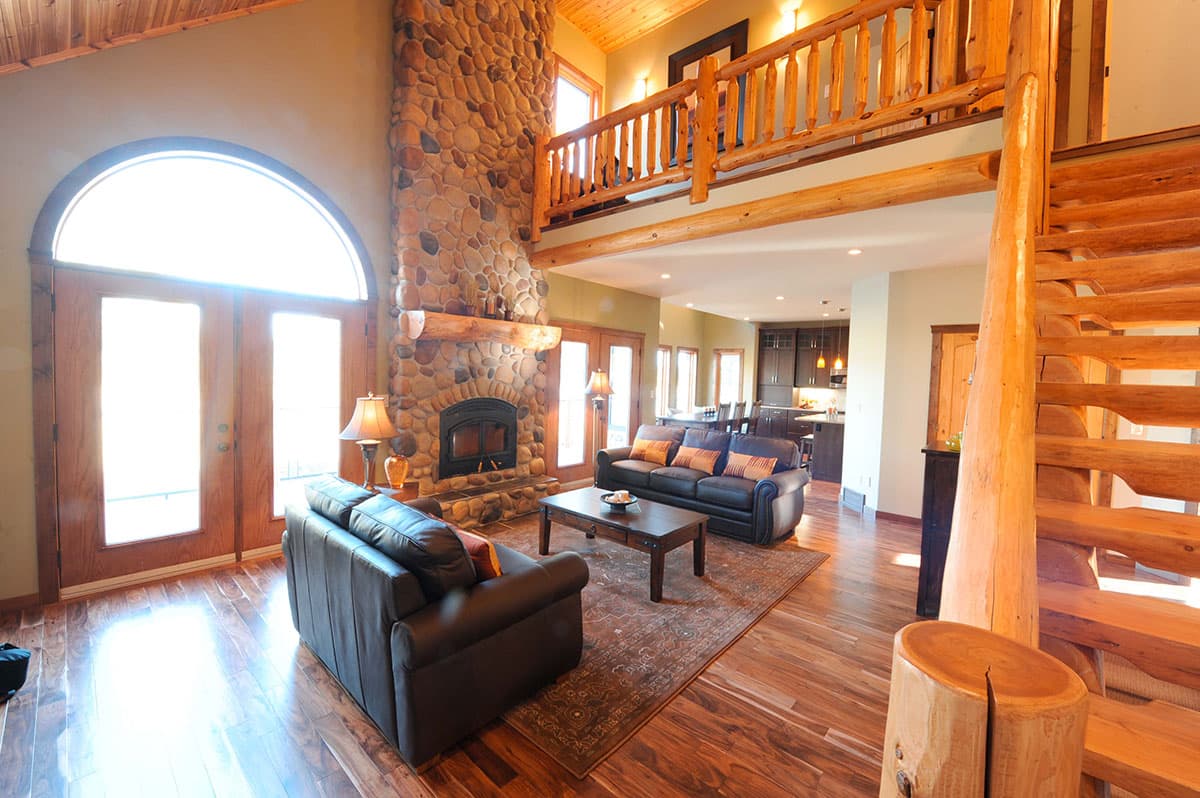Great room with stone fireplace, lofted second story with log railing, and open kitchen.