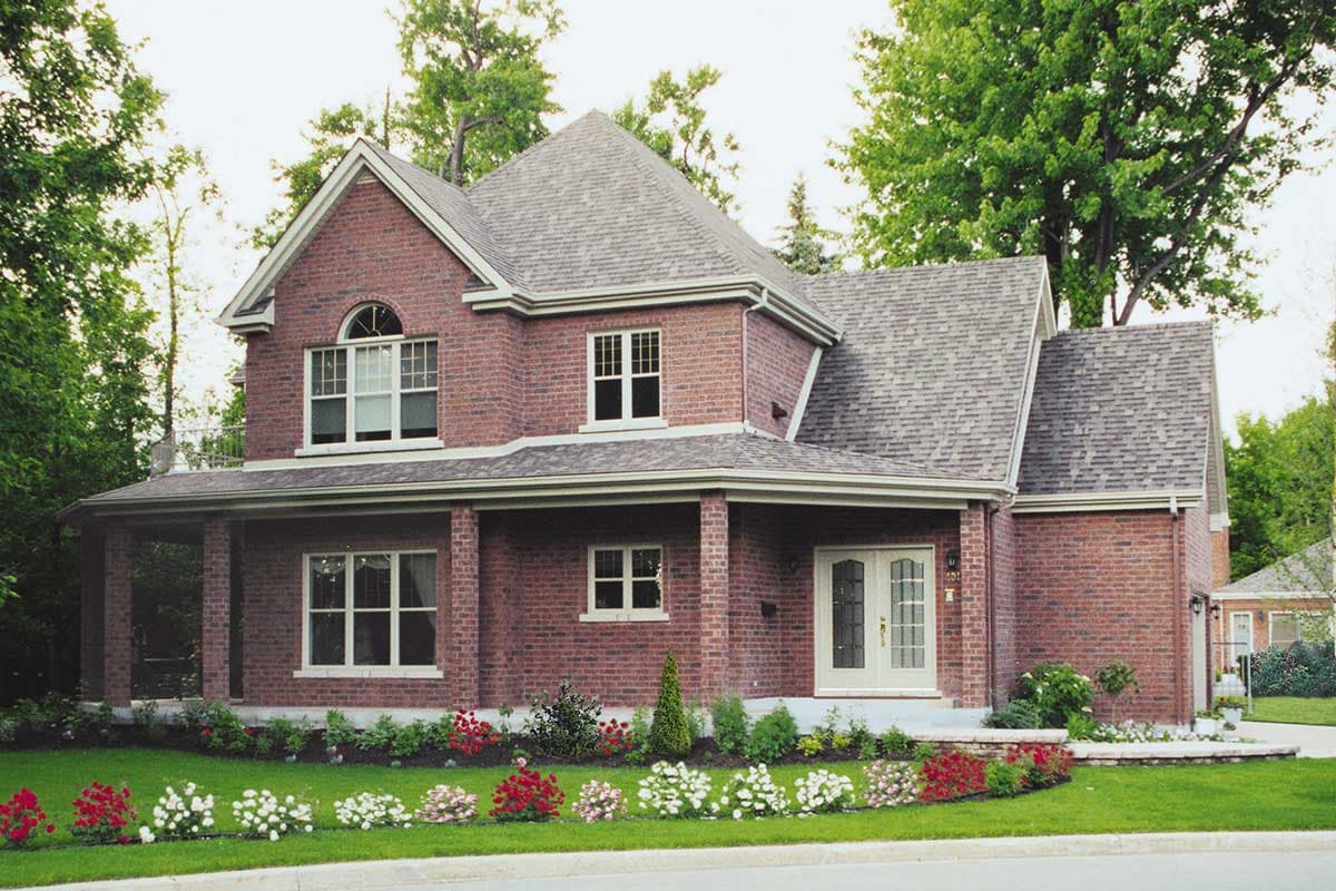 Two-story brick house plan exterior with covered porch, arched window, gabled roof, and varied rooflines.