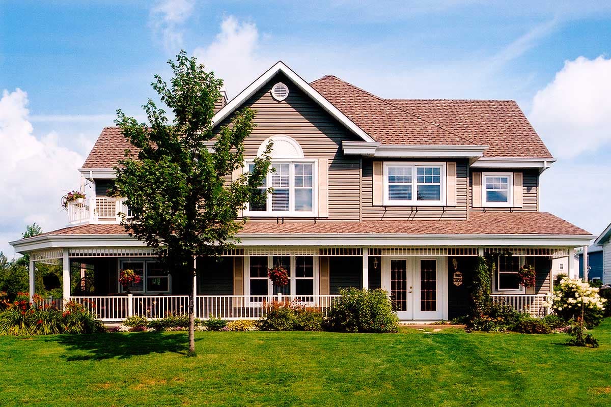 House plan exterior: Two-story home with wrap-around porch, gabled dormers, and arched window.