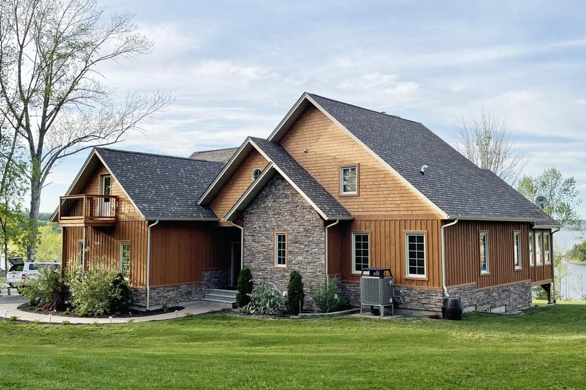 House plan exterior: Two-story home with wood siding, stone accents, prominent gables, and a second-story balcony.