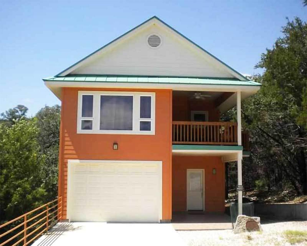 House plan exterior: Two-story structure with attached garage, prominent gable roof, upper-level balcony, and large upper-level window.