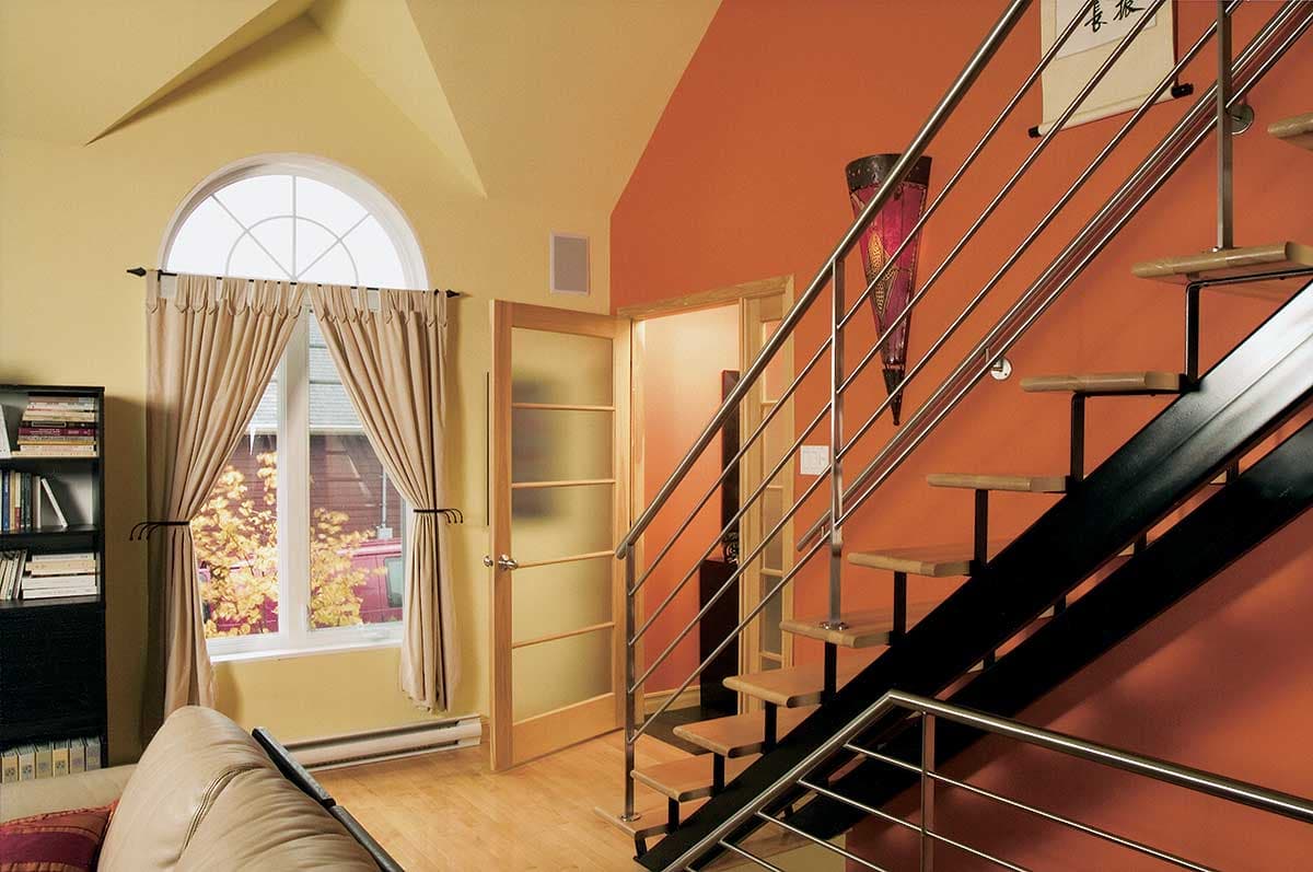Interior view of a modern staircase with wood treads and metal railings, next to a tall window with an arched transom.