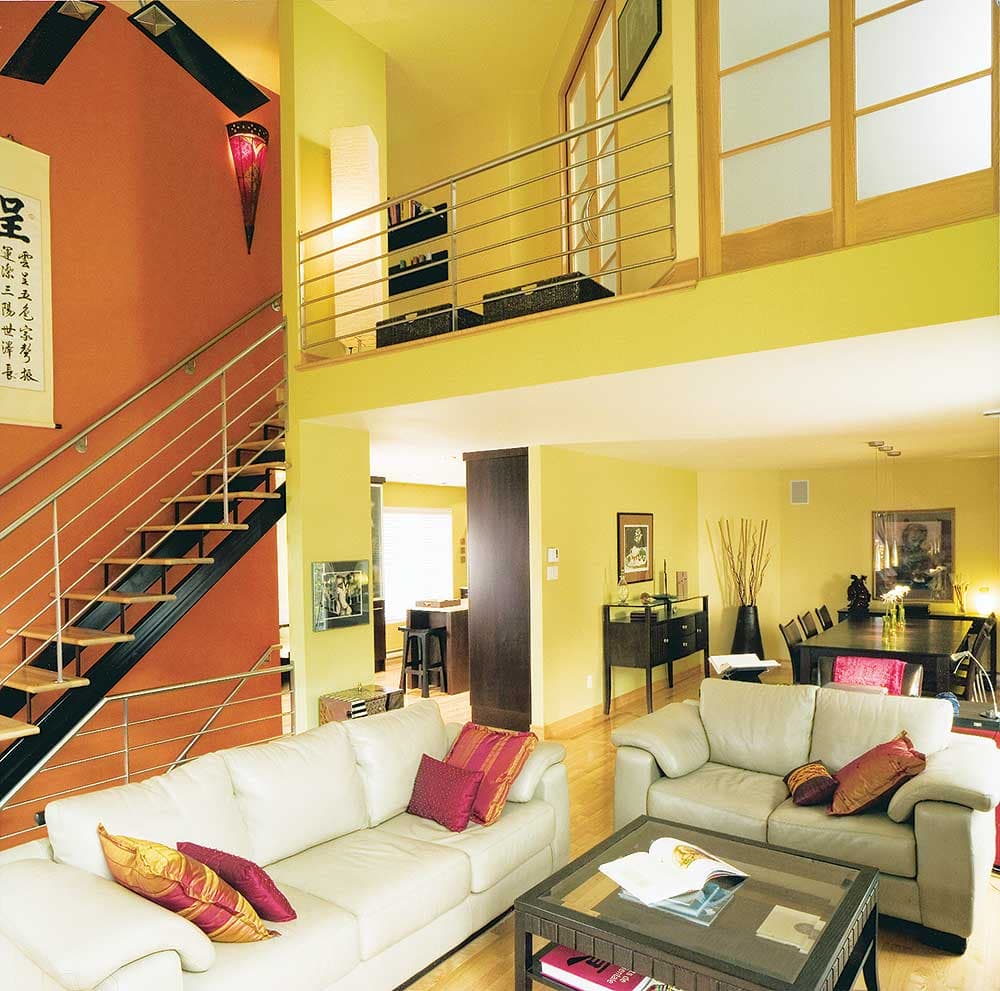 Interior view of open-concept living and dining areas with a floating staircase, mezzanine, and kitchen visible.