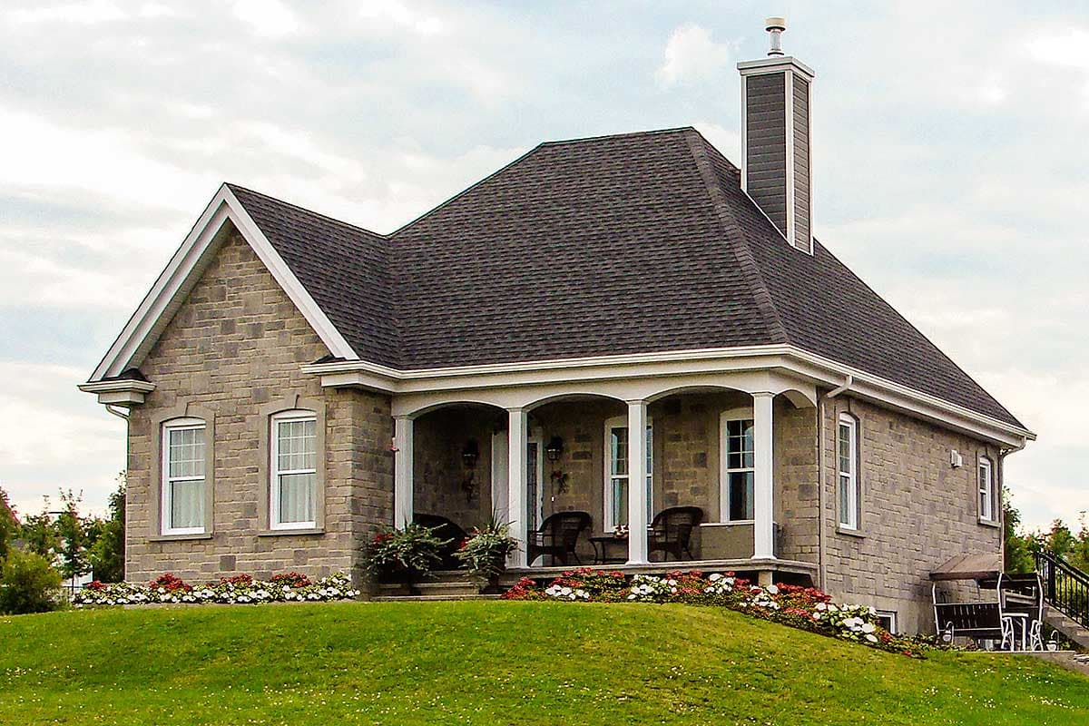 House plan exterior: Stone-clad residence with a covered porch supported by columns, gabled dormers, and a prominent chimney.