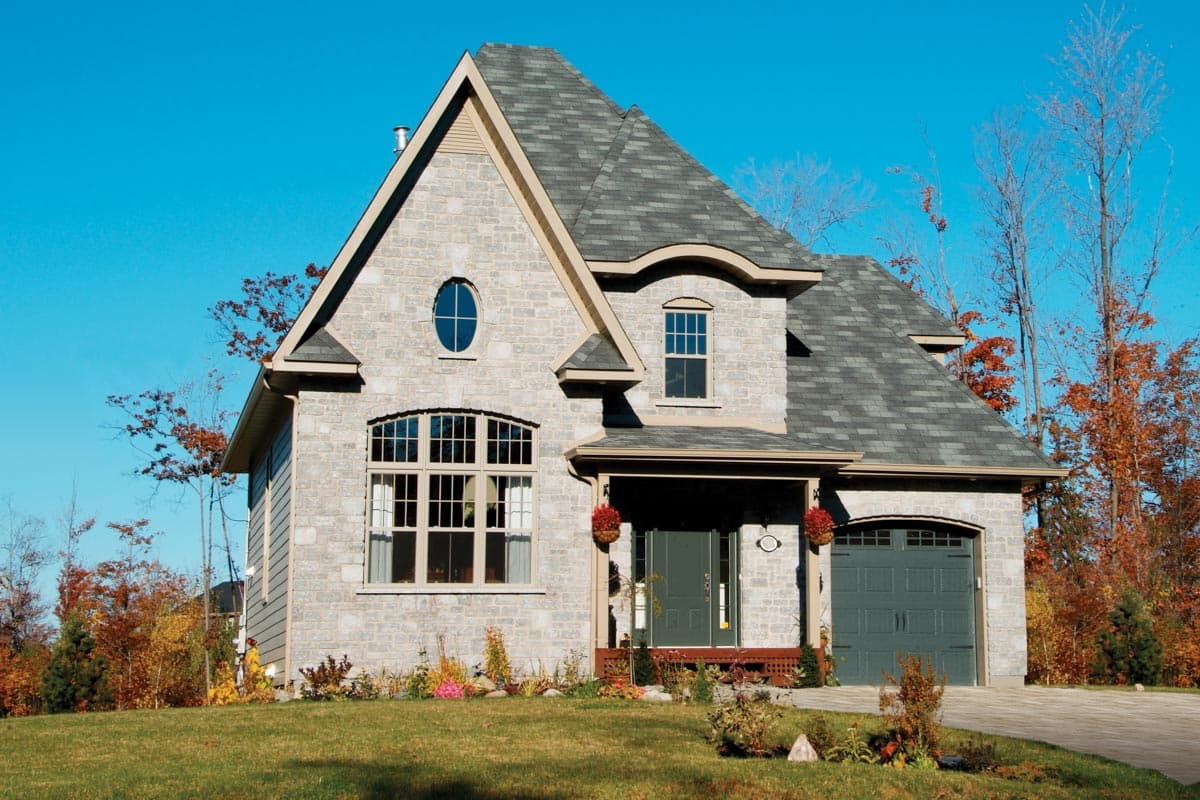 Two-story house plan exterior with stone facade, gabled dormer, arched window, oval window, and attached garage.