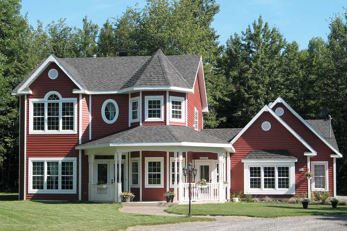 House plan exterior: Two-story red house with a wraparound porch, gables, and an octagonal turret.