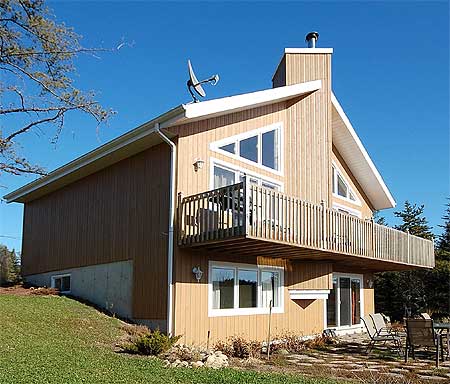 House plan exterior featuring a two-story design with a prominent upper-level balcony, vertical siding, and a gabled roofline with triangular windows.