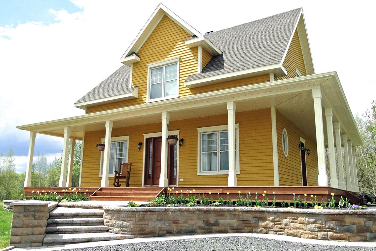House plan exterior. Two-story farmhouse with a wraparound porch supported by columns. Features include gabled roof and dormer.