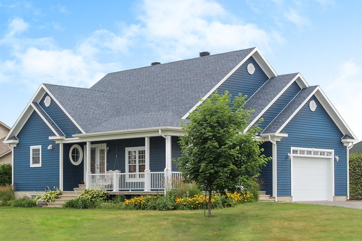 House plan exterior: Blue siding, gabled roof, covered porch with white railings, and attached two-car garage.