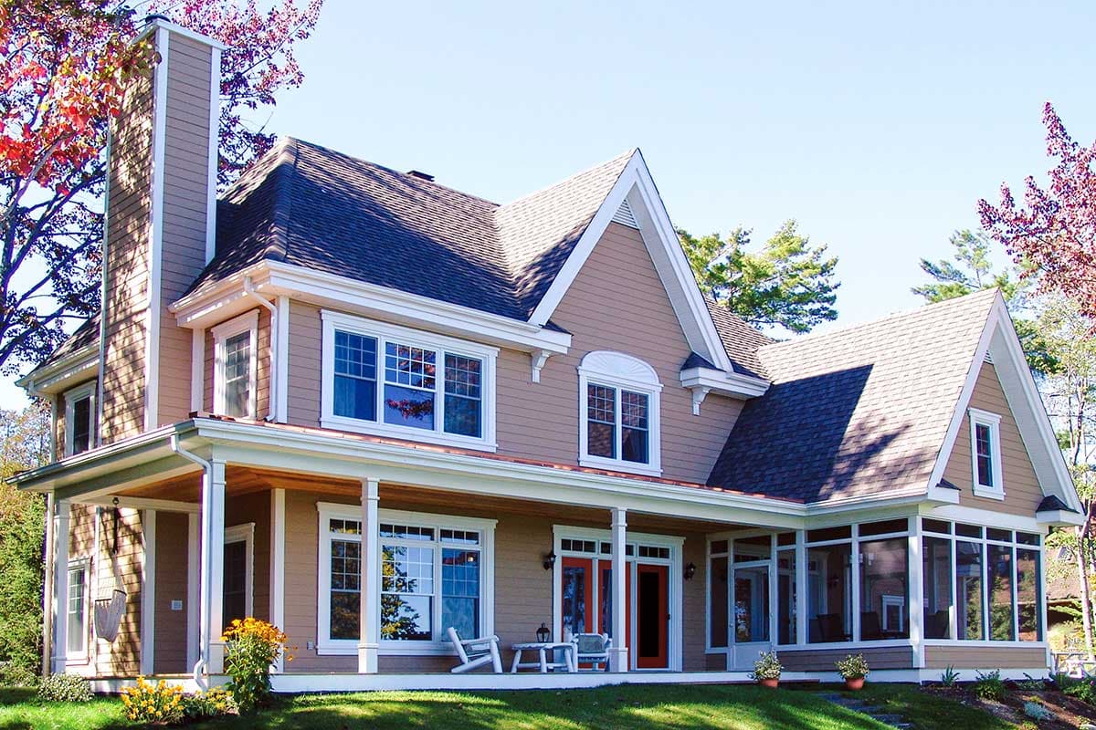House plan exterior: Two-story home with wrap-around porch, prominent stone chimney, and multiple gables.