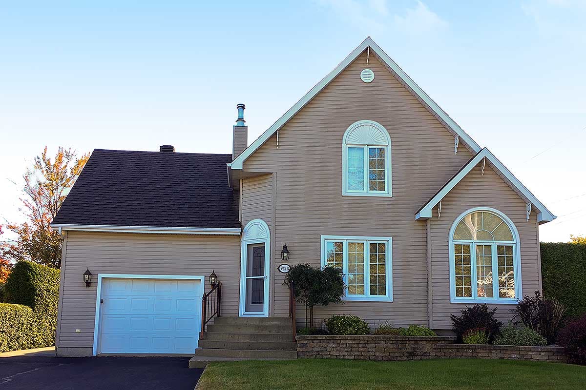 House plan exterior showing a two-story home with vinyl siding, arched windows, prominent gables, and an attached garage.