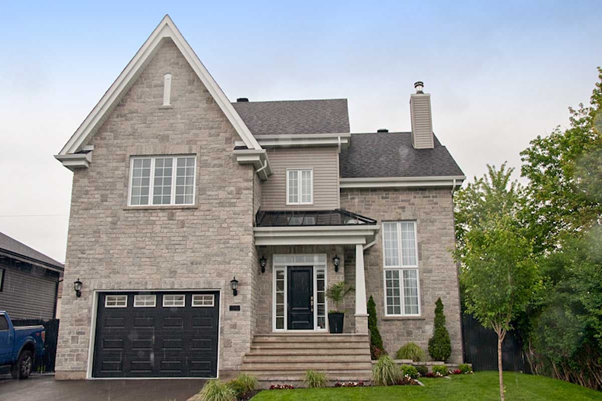 Two-story house plan exterior with stone facade, prominent gable, covered entry with columns, and attached garage with six windows.