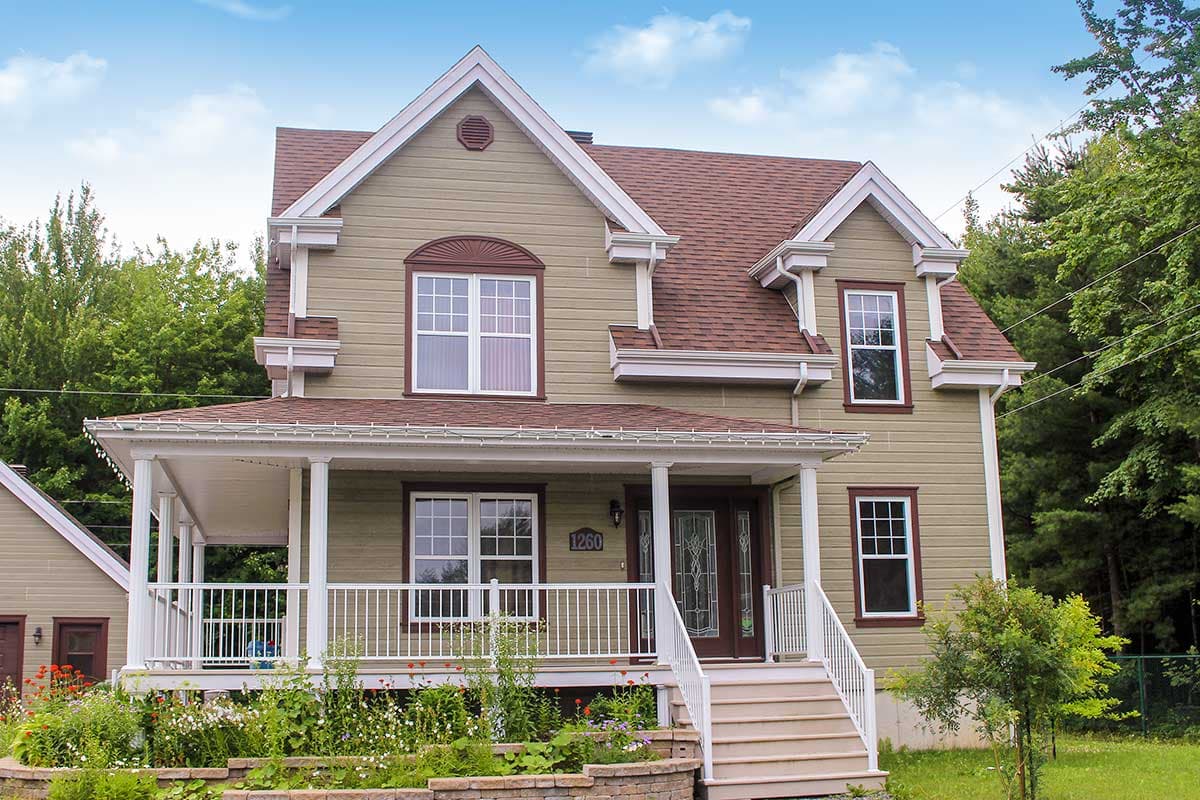 House plan exterior: Two-story home with a wrap-around porch, gabled dormers, and a prominent central gable.