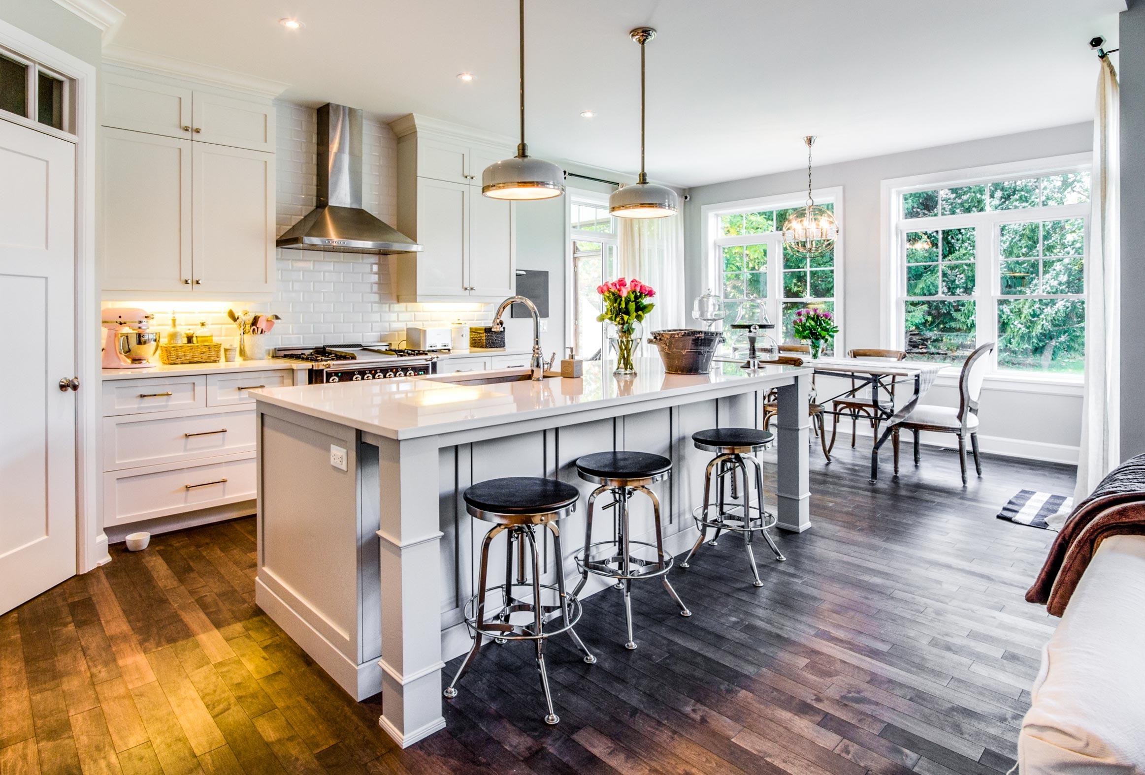 Kitchen with island, pendant lights, subway tile backsplash, stainless steel range hood, and dining area with large windows.