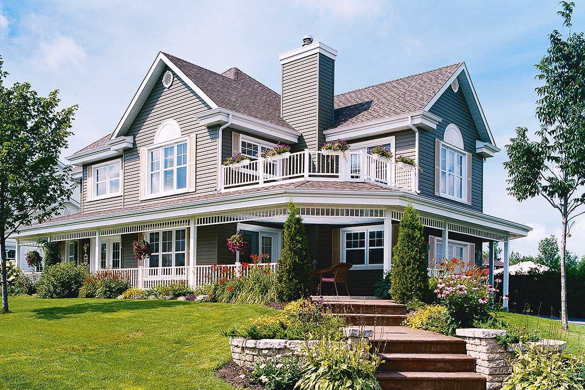 Two-story house plan exterior with wraparound porch, upper balcony, gables, and arched windows.