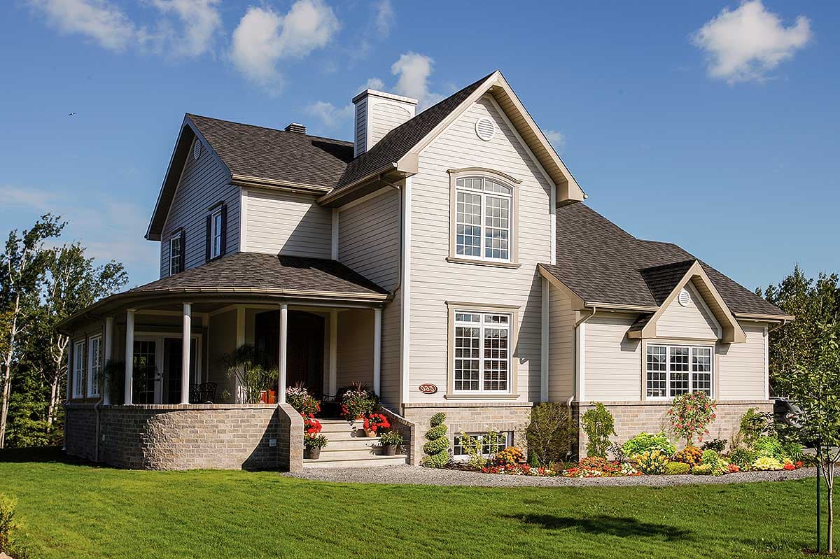 House plan exterior: Two-story home with a wraparound porch, brick foundation, multiple gables, and arched window.