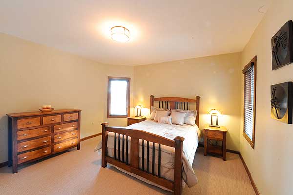 Bedroom with wooden bed, dresser, and two nightstands. Windows with blinds and wall art.