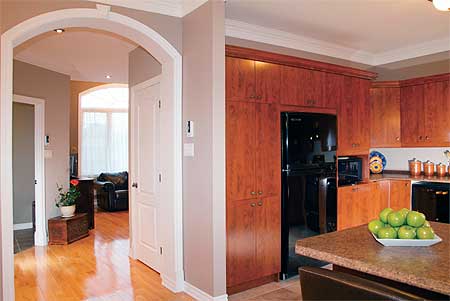 View of kitchen with wood cabinets and black appliances, adjacent to a hallway with arched doorway.