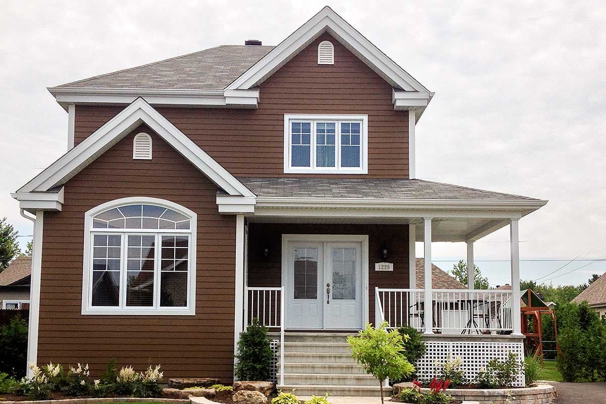 House plan exterior: Two-story home with a covered front porch, white railings, gabled dormers, and a large arched window.
