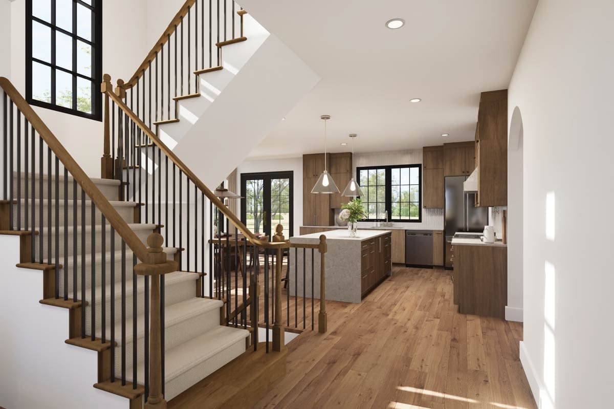 Spacious, modern home interior with a grand staircase and open-concept kitchen. Wooden floors flow from stairs into the kitchen area.