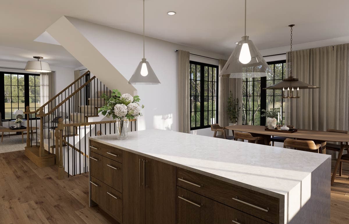 A modern kitchen with a large island, wooden cabinets, and a staircase leading to the upper floor. Large windows offer a view of the outdoors.