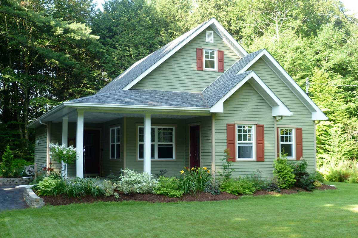 House plan exterior: two-story cottage with gabled dormers, covered front porch supported by white columns, and green siding with red shutters.