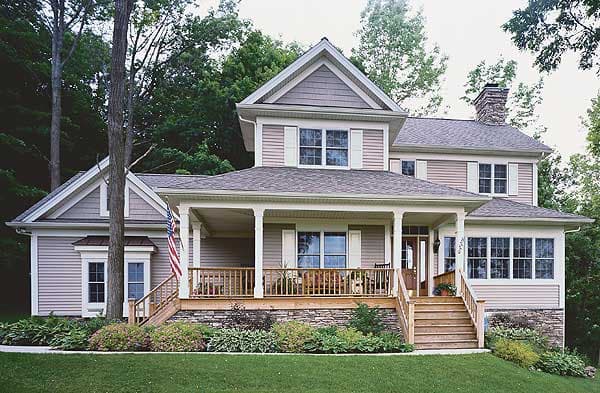 House plan exterior: Two-story home with a wraparound porch, stone foundation, and prominent gables.