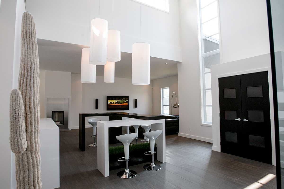 Interior view of a modern home with a double-height ceiling, contemporary bar seating, fireplace, and black double doors.