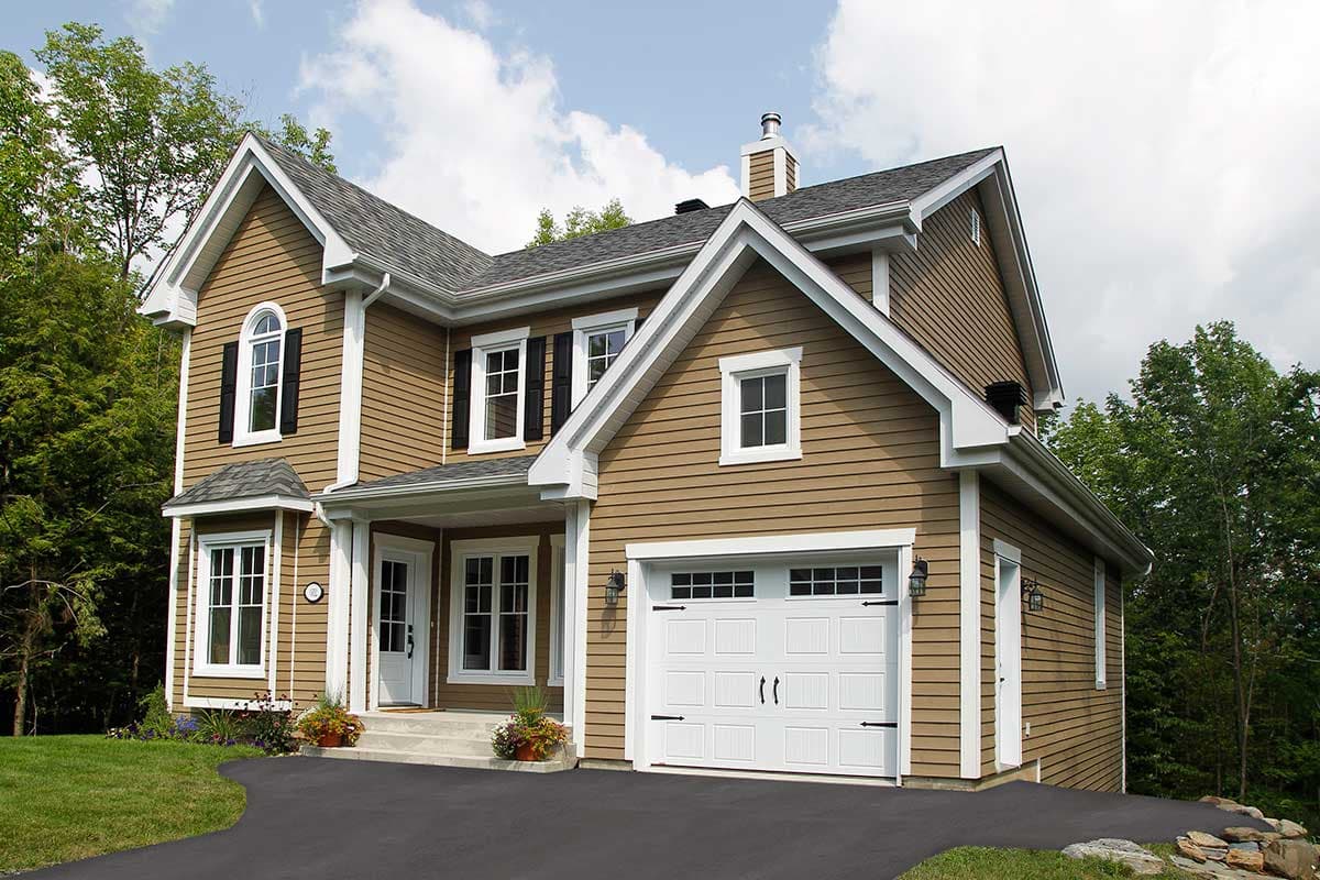 House plan exterior: Two-story, tan siding, gabled roof, prominent dormer, and attached front-facing garage.