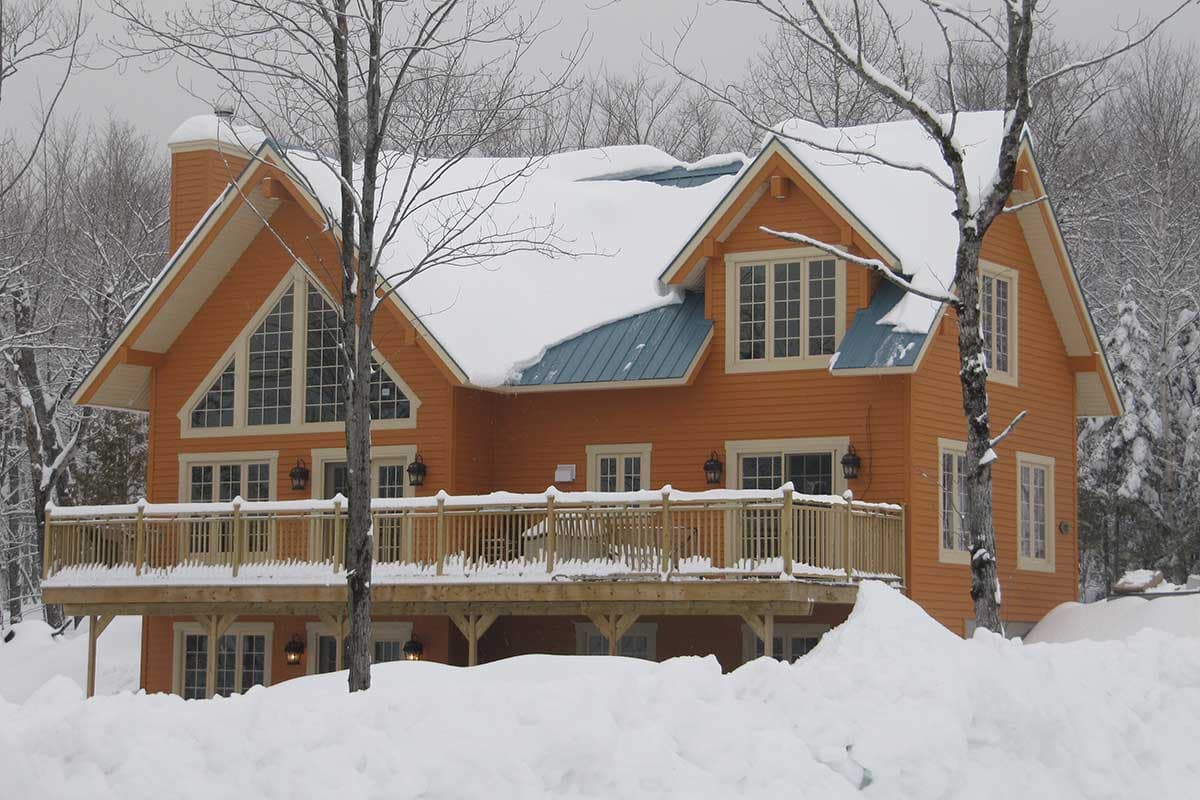 House plan exterior: two-story home with large deck, gabled dormers, and a prominent triangular window feature.