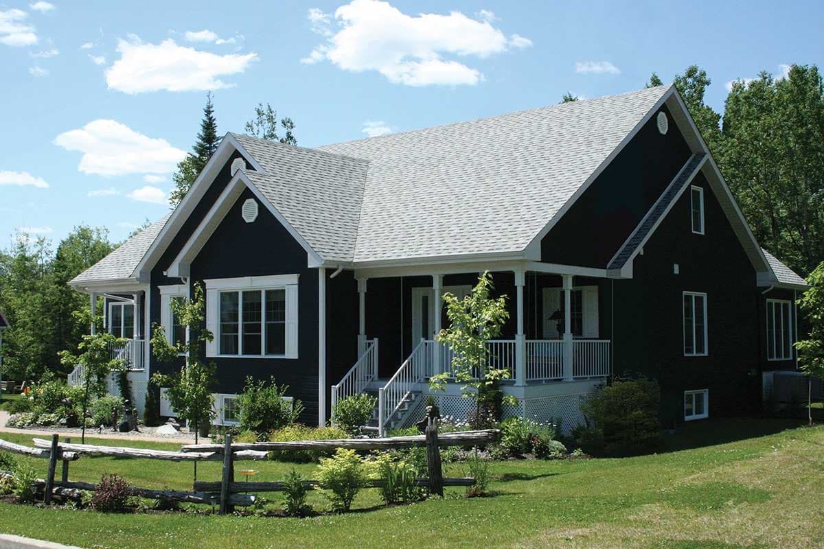 House plan exterior: Dark siding, one-story home with a gabled roof, wraparound porch, and front entrance.