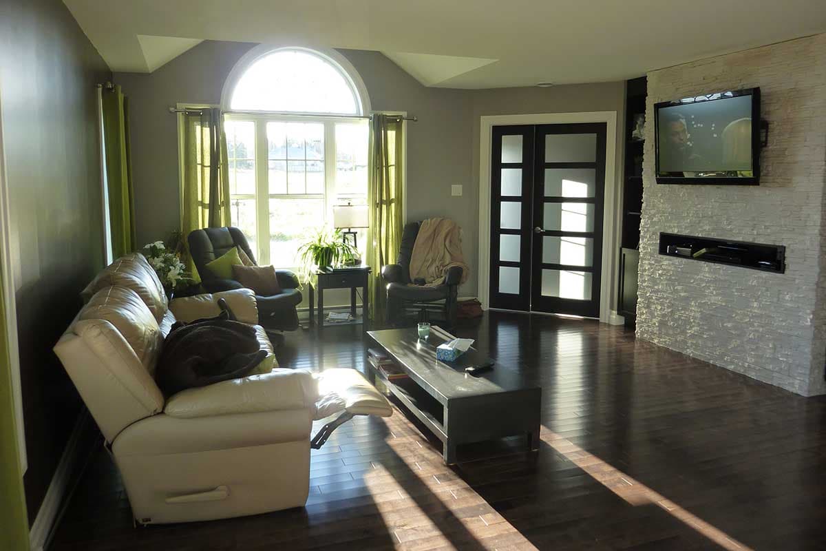 Living room with vaulted ceiling, arched window, double doors, and stone-clad fireplace with television.