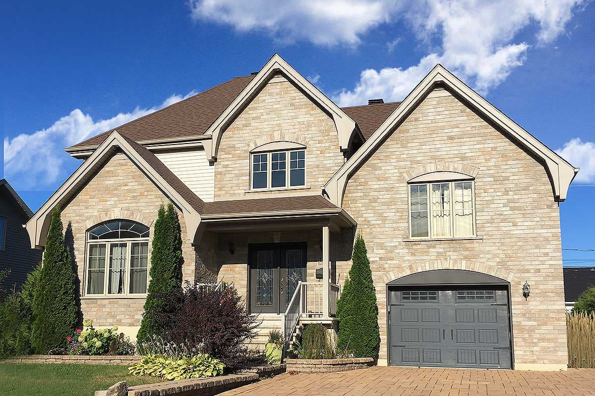 House plan exterior. Two-story home with brick facade, multiple gables, arched windows, and a front-facing garage with a dark gray door.