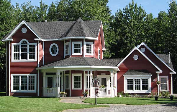 House plan exterior: Two-story red house with a wraparound porch, multiple gables, and arched window detail.