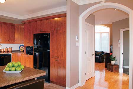 Interior view of kitchen with wood cabinetry and black refrigerator, opening to a hallway with an arched doorway.