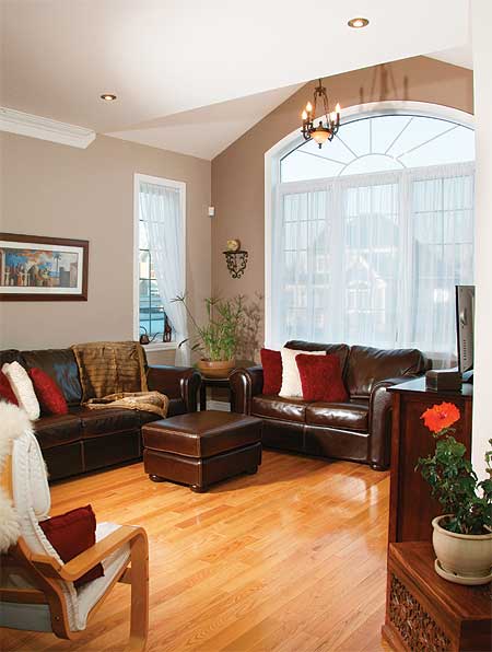 Living room with leather sofas, ottoman, and vaulted ceiling featuring a large arched window with white drapes.