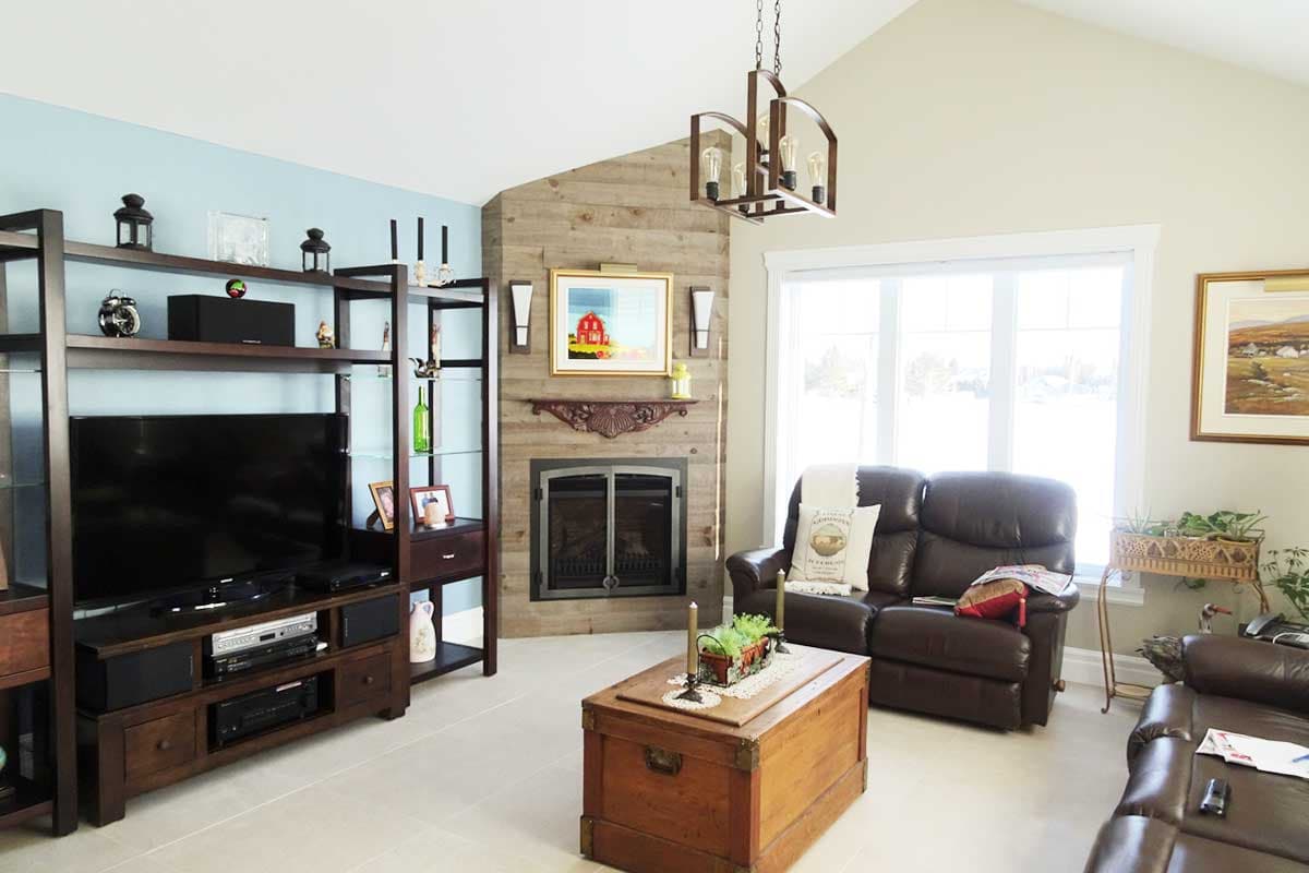 Living room with vaulted ceiling, wood-paneled corner fireplace, entertainment center, and leather sofas.
